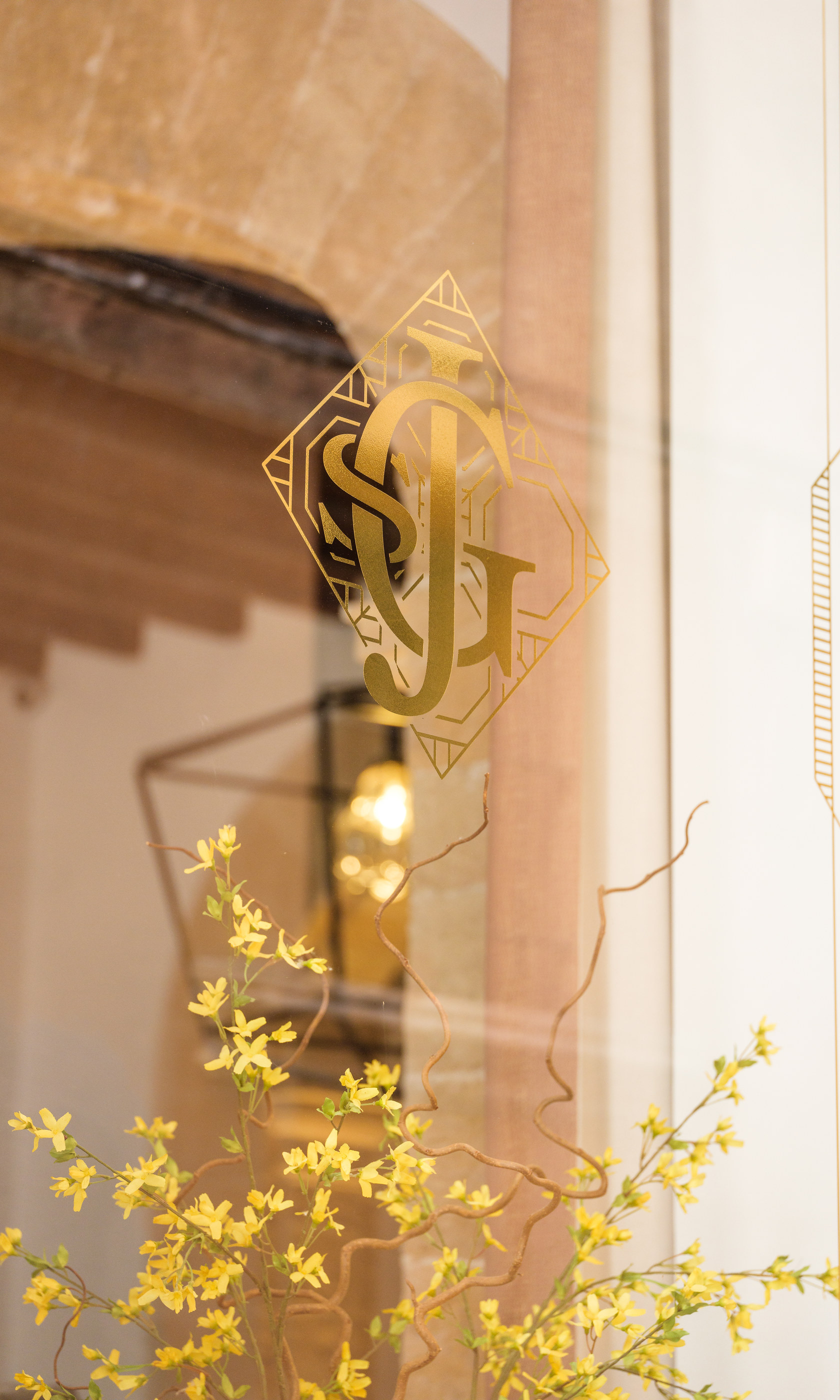 The Glòria monogram on a window with yellow flowers